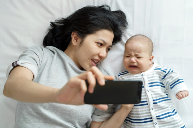 Asian Young Mother comforts her Newborn baby son while crying lying on bed.